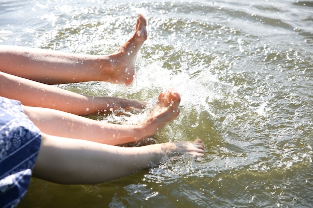 川で足を洗う裸足の女性。湖の近くの美しい女の子。休日を楽しんでいる友達。素朴な夏のフラットレイ。木製の橋。晴れた日はリラックスしてください。