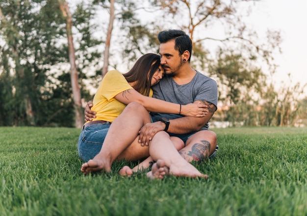 Barefoot young couple sitting and embracing in park. Loving couple having a good time in the park.