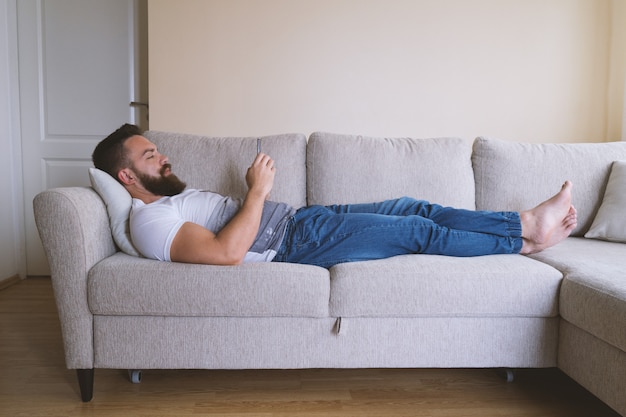 Barefooted hipster lying on sofa with smartphone