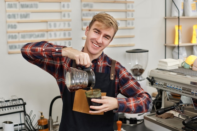 エプロンのバリスタが淹れたてのコーヒーをカップに注ぐ