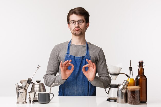 Barista, cafe worker and bartender concept. Portrait of impressed, pleased caucasian man, employee in apron and glasses make not bad sign, show okay in confirmation, approve good coffee making method