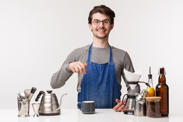 Barista, cafe worker and bartender concept. Young caucasian guy working at restaurant, mixing drinks, standing near teapot, chemex, prepare filter coffee, 