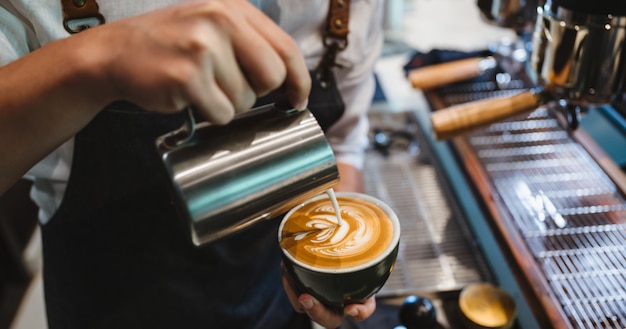 Barista die latte kunst, schotnadruk in kop van melk en koffie maakt