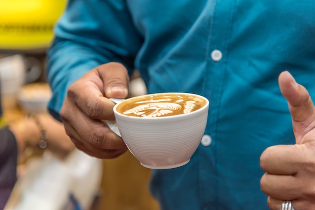 Barista die latte schuim gieten om een ​​koffie latte kunst in de witte koffiekop te maken