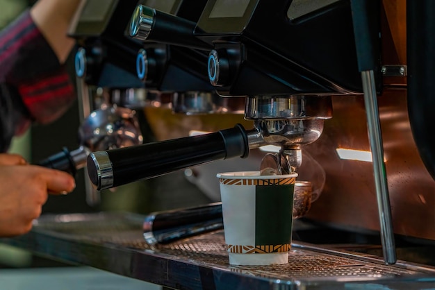 バリスタがミルクを泡立ててコーヒーを作る バリスタがコーヒーマシンの前で手を組む