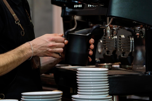 Barista frothing milk to make coffee Barista hands in front of coffee machine