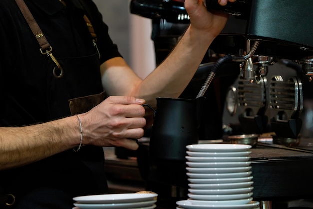 Barista frothing milk to make coffee Barista hands in front of coffee machine