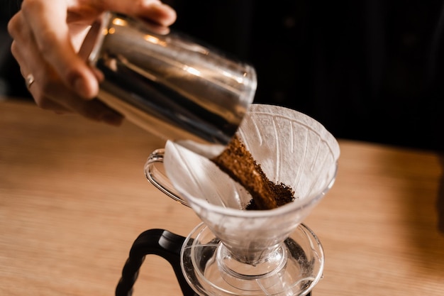 Barista giet gemalen koffie over papieren filter voordat water uit druppelketel wordt gegoten. Proces van brouwen giet over filterkoffie in café