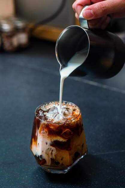 Barista giet melk in een glas ijskoffie