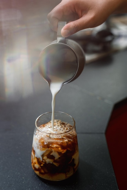 Barista gieten melk in een glas ijskoffie