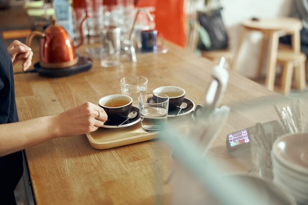 Barista che dà ordine al cliente presso la caffetteria alla moda. due tazze di caffè con bicchieri d'acqua.