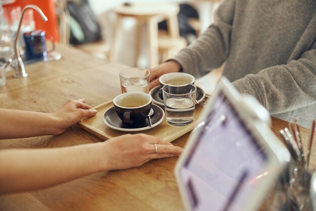 Barista giving order to client at the trendy coffee shop. Two cup of coffee with glasses of water.