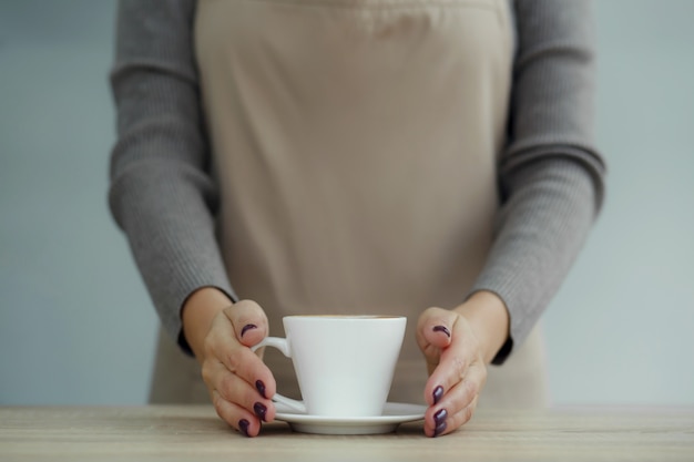 喫茶店のエプロンに入ったバリスタが淹れたてのコーヒーをお客様にお渡しします