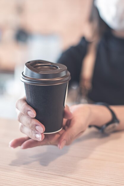 Barista in schort en gezichtsmasker staat achter de toonbank klaar om koffieservice te geven in de winkel