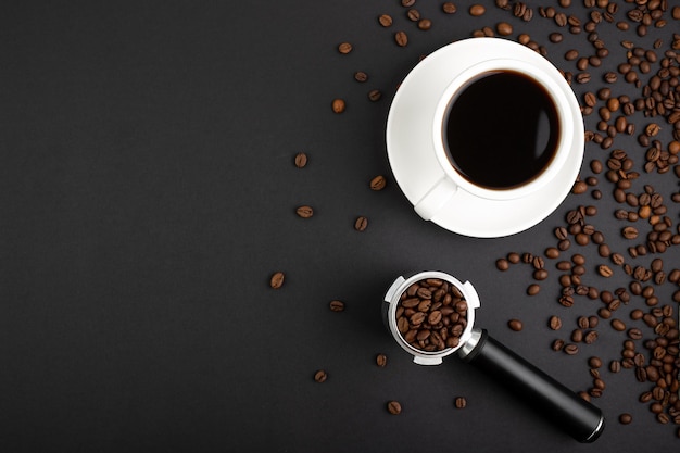 Barista Kit coffee horn with coffee beans and white cup filter flatlay on black background with roasted beans Barman tool for pressing down ground coffee a tamper for a coffee machine