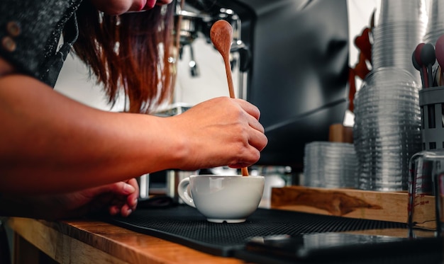 Фото Бариста готовит кофе деревянной ложкой, готовит или готовит кофейную пену в чашке кофе