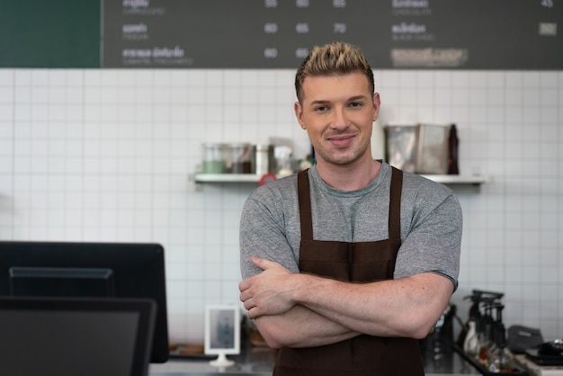 Foto barista uomo braccia incrociate in piedi dietro la macchina del caffè al bar