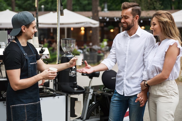 Foto barista man koffie te verkopen aan jong koppel in de verplaatsbare coffeeshop op straat