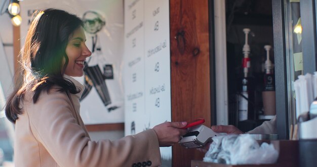 바리스타 남자는 무접촉 휴대전화로 신용카드 시스템에 지불하는 여성 고객을 위해 테이크아웃 커피를 만듭니다.