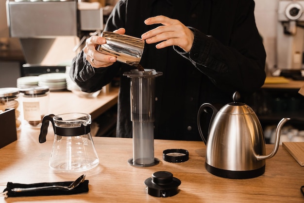 Barista pour ground coffee over aeropress before pouring water from drip kettle Process of brewing aeropress coffee in cafe