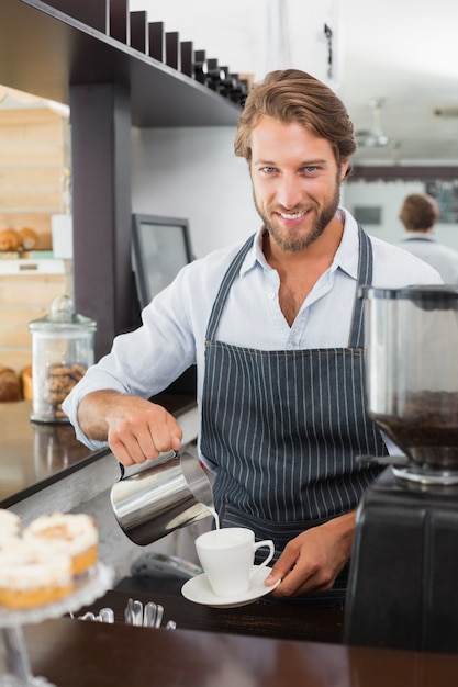 Barista pouring milk into cup of coffee 