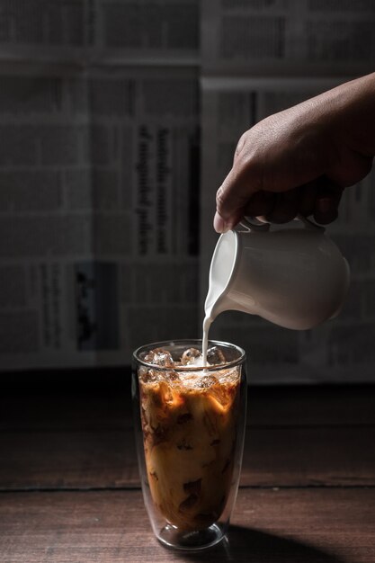 Barista pouring milk into a glass of iced coffee