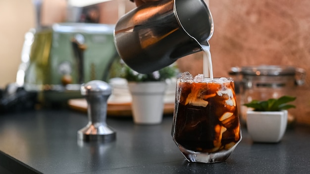 Barista pouring milk into a glass of iced coffee