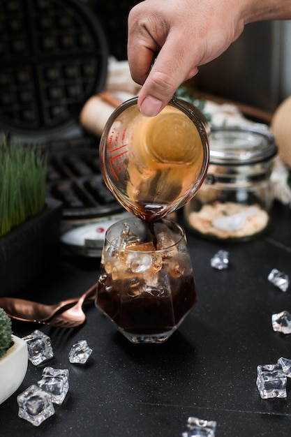 Barista pouring milk into a glass of iced coffee