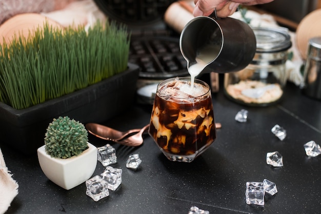 Barista pouring milk into a glass of iced coffee