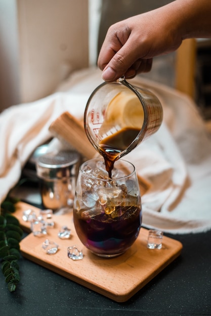 Barista pouring milk into a glass of iced coffee