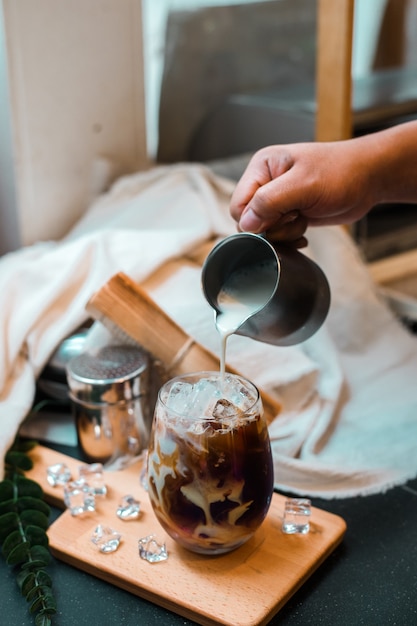 Barista pouring milk into a glass of iced coffee