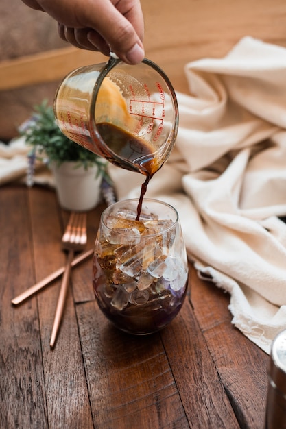 Barista pouring milk into a glass of iced coffee