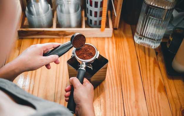 バリスタがコーヒー豆焙煎機の粉末挽いたコーヒーをポルタフィルターに注ぐ