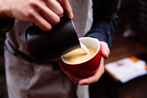 Barista pours fresh milk into a cup of coffee latte art