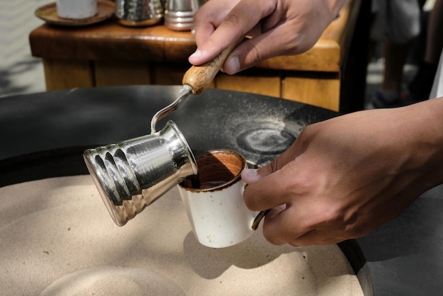 Il barista versa il caffè turco appena fatto sulla sabbia in un cezve in un primo piano della tazza un barista professionista prepara il caffè a mano in modo tradizionale spazio di messa a fuoco selettiva per il testo