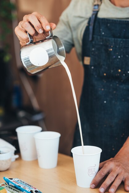 The barista pours milk from a tin can into coffee in a paper disposable cup