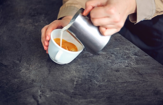 Foto il barista versa il latte montato nella tazza per il cappuccino. focalizzazione morbida.