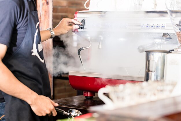 Barista preparing coffee at steaming machine in cafe