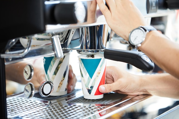 Barista's hands pouring coffee into a glass from a coffee machine