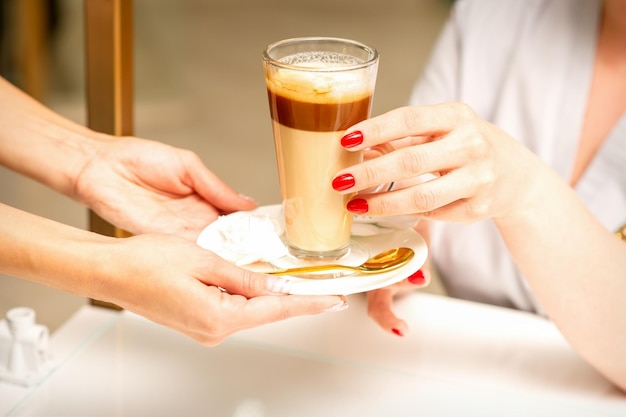 Barista serving coffee latte in glass mug for a customer close up hands