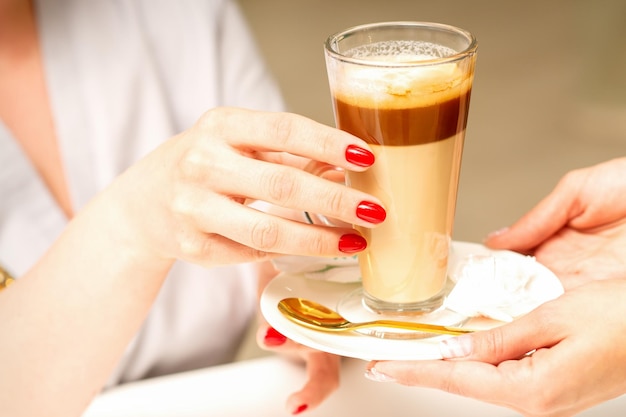 Barista serving coffee latte in glass mug for a customer close up hands