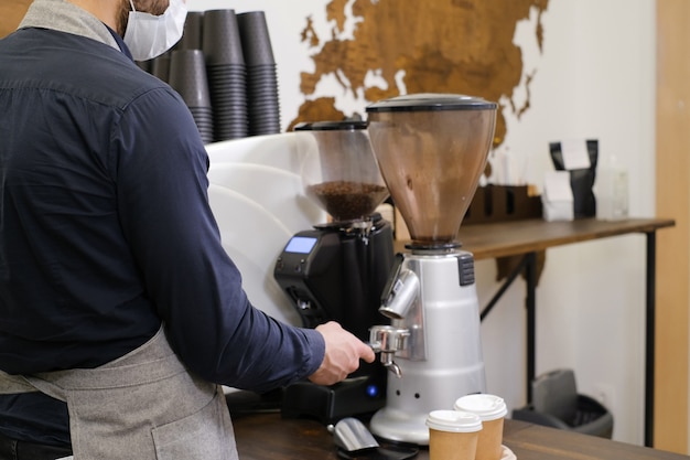 Barista serving coffee in takeaway cups in coffee shop in mask