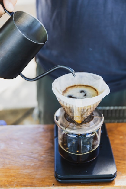 Barista spills hot water prepare filtered coffee from stainless steel teapot to drip paper maker on black simple weights.