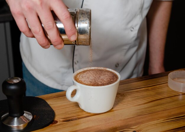 Barista sprinkling chocolate on coffee in cafe