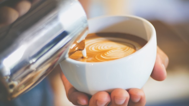 barista stromende gestreamde melk om latte kunst van de hartvorm te maken