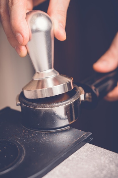 Barista tampering coffee in portafilter using tamper Closeup fresh coffee preparation process