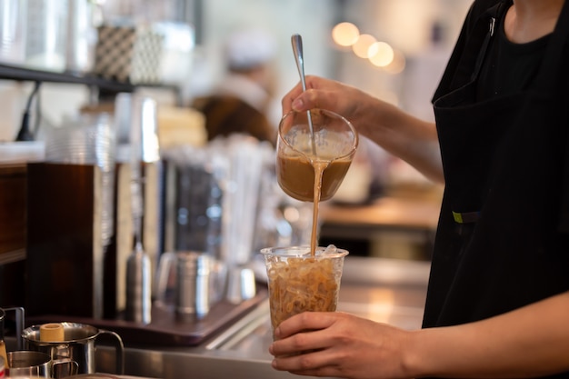 Barista Vrouw barista koffie gieten in afhaalmaaltijden glas in de koffieshop.