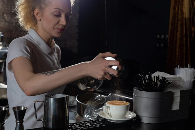 Barista vrouw hand bestrooit kaneel op koffie cappuccino of latte op toog in café