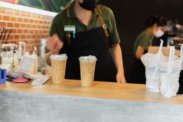 Barista wearing face mask serving iced coffee drink to customer in cafe