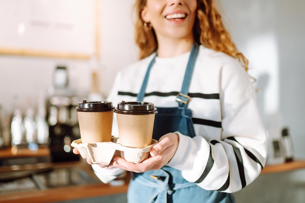 Una donna barista in grembiule tiene in mano il caffè caldo in un bicchiere di carta